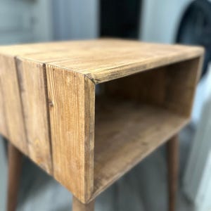 May include: A wooden end table with a single shelf and tapered legs. The table is made of natural wood with a light brown finish.