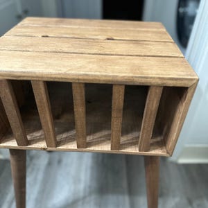 May include: A wooden end table with a slatted shelf and four legs. The table is stained a light brown color.