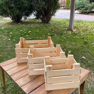 May include: Three wooden crates of varying sizes, stacked on a wooden table. The crates are made of natural wood and have a rustic look.