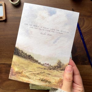 May include: A rectangular art print featuring a watercolor landscape of a golden field, green trees, and a small house under a cloudy sky. The text reads: FOR THY MERCY IS GREAT UNTO THE HEAVENS, AND THY TRUTH UNTO THE CLOUDS. Psalm 57:10.