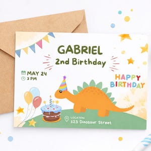 May include: A birthday invitation featuring a cartoon orange dinosaur wearing a party hat. The invitation reads "Gabriel 2nd Birthday" with the date, time, and location. Includes a brown envelope, party hat, and confetti.
