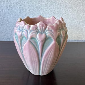 May include: A pink and green ceramic vase with a floral design. The vase is shaped like a flower and has a scalloped rim.