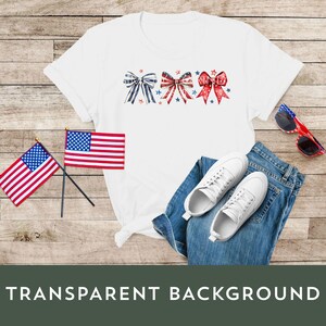 K&ouml;nnte beinhalten: Wei&szlig;es T-Shirt mit drei roten, wei&szlig;en und blauen Schleifen. Die Schleifen sind horizontal in der Mitte des Shirts angeordnet. Das Shirt liegt auf einer Holzoberfl&auml;che mit zwei amerikanischen Flaggen und einem Paar wei&szlig;en Sneakers.
