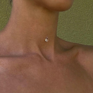 Puede incluir: Un collar gargantilla transparente con un colgante de cristal en forma de lágrima.