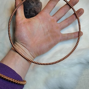May include: A copper wire hoop, twisted and coiled, is held in a hand. The hoop is about 20 cm in diameter.