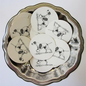May include: A set of eight white paper coasters with black and white illustrations of a dog breed. The coasters feature a stylized illustration of a dog with a long, pointed nose and floppy ears.