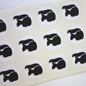 May include: Sheet of white paper with 12 black silhouette stickers of a person with long hair in a ponytail. The stickers are arranged in a grid pattern.