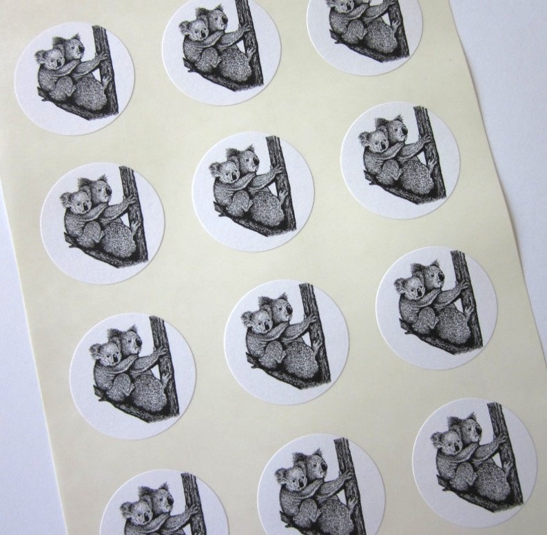 May include: A sheet of white paper with 12 round stickers featuring black and white illustrations of two koalas hugging on a tree trunk.