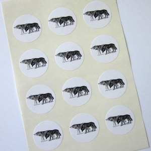 May include: A sheet of white paper with 12 round stickers featuring black and white illustrations of wolves. Each sticker has a wolf walking to the right.
