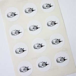 May include: Sheet of white paper with 12 round stickers featuring a black and white illustration of a sleeping fox.