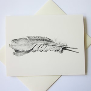 May include: A greeting card featuring a detailed black and white illustration of a feather. The feather is drawn with fine lines, showcasing its texture and shape. The card is cream-colored and is placed on top of a matching envelope.