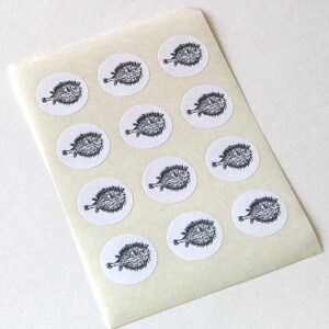 May include: A sheet of white sticker paper with 12 black and white illustrations of pufferfish. The stickers are round and have a white background.