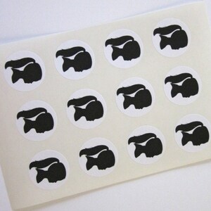 May include: A sheet of white sticker paper with 12 black silhouette stickers of a girl with a ponytail. Each sticker is a circle with a white background.