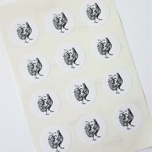 Peut inclure: Une feuille de papier autocollant blanc avec 12 illustrations de coqs en noir et blanc. Chaque coq est imprimé sur un autocollant rond.