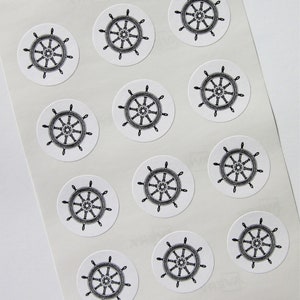 May include: A sheet of circular stickers with a black and white ship's wheel design. The nautical stickers are on a white background. The image is a close-up, showing several stickers.