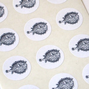 May include: A sheet of white paper with multiple round stickers featuring black and white illustrations of pufferfish.