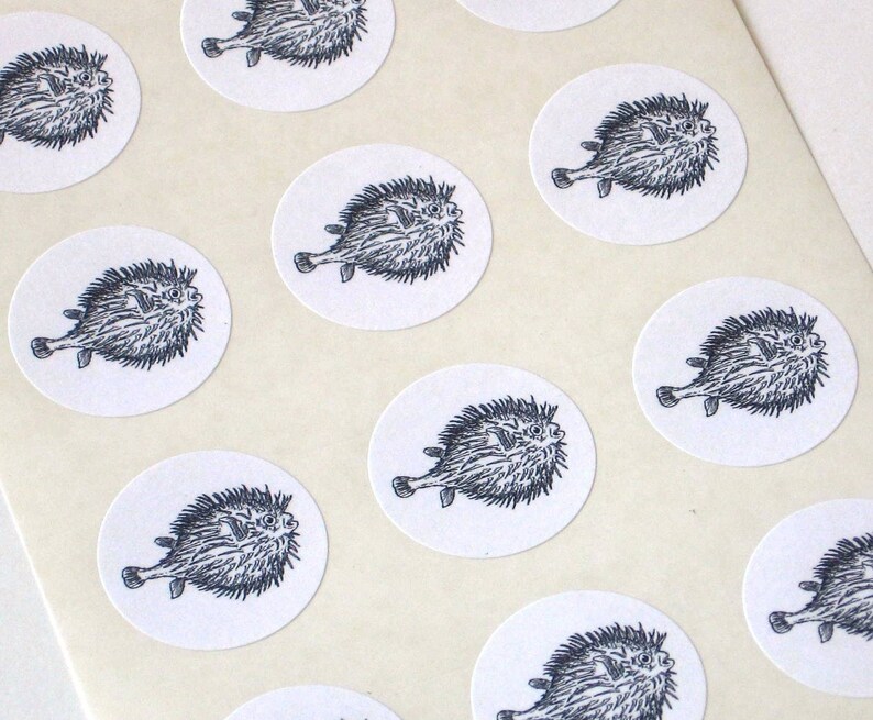 May include: A sheet of white paper with multiple round stickers featuring black and white illustrations of pufferfish.