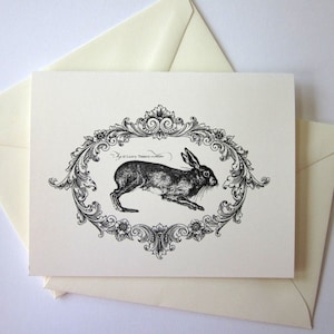 Peut inclure: Illustration en noir et blanc d'un lapin dans un cadre orné. Le lapin court vers la droite et le cadre est décoré de motifs floraux et de volutes.