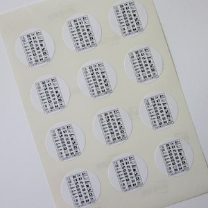 Puede incluir: Una hoja de papel blanco con doce pegatinas redondas. Cada pegatina presenta un gráfico en blanco y negro de una bandera náutica.