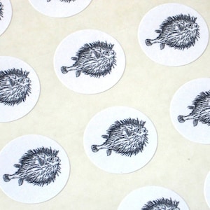 May include: A sheet of round stickers featuring black and white illustrations of pufferfish. Each sticker has a white background and a black outline.