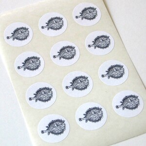 May include: A sheet of white paper with 12 round stickers featuring black and white illustrations of pufferfish.