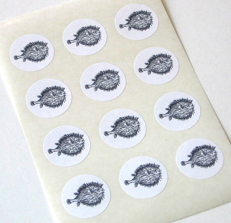 May include: A sheet of white paper with 12 round stickers featuring black and white illustrations of pufferfish.