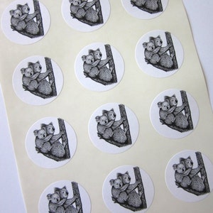 May include: Sheet of 12 round stickers featuring black and white illustrations of two koalas cuddling on a tree branch.