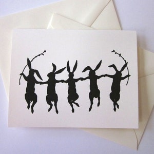 May include: A greeting card with a black silhouette of five rabbits dancing in a circle. The rabbits are holding hands and have long ears. The card is white with a black border.