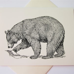 May include: A black and white illustration of a bear on a cream-colored card. The bear is depicted in a detailed, cross-hatch style, with its paw touching the ground. The card is placed on top of a cream-colored envelope.