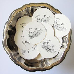 May include: A silver serving bowl filled with round paper coasters featuring black and white illustrations of geese. The coasters have a white background and black outlines of the geese.