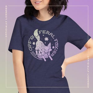 Puede incluir: Camiseta azul marino con una ilustración en morado claro de un zorro y el texto "GPF'S FERAL FOXIES" en un círculo. La camiseta tiene mangas cortas y cuello redondo. Las palabras "OFFICIALLY LICENSED" están impresas verticalmente a izquierda y derecha.