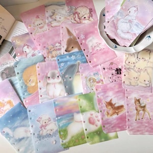 以下が含まれることがあります： ピンク、青、白を基調とした、可愛らしい動物のイラストが描かれた装飾的なプランナー用リフィル。ウサギ、子羊、鹿など、様々な動物がソフトなパステル調で描かれています。各リフィルには、整理しやすいように穴が開いています。
