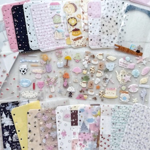May include: A collection of decorative stickers and planner inserts. The stickers feature various designs, including houses, desserts, flowers, and coffee cups. The planner inserts have different patterns, such as stars, dots, and floral designs. The color palette includes pink, white, and pastel colors.