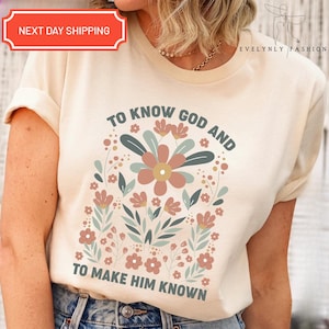 May include: Cream-colored t-shirt with a floral design and the text "TO KNOW GOD AND TO MAKE HIM KNOWN." The design features a large central flower with surrounding smaller flowers and leaves in muted colors. The shirt also has the text "NEXT DAY SHIPPING."