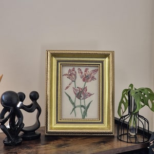 May include: A framed print of a botanical illustration featuring red and pink tulips with green stems and leaves. The frame is gold with a decorative border.