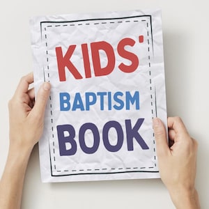May include: A white, crumpled paper with the words "KIDS' BAPTISM BOOK" in red, blue, and purple. The text is inside a black dashed-line border. The paper is held by two hands against a white background.