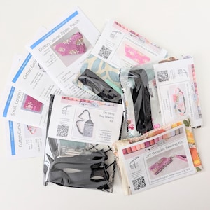 May include: A collection of DIY sewing kits, including a zipper pouch, sling bag, and wristlet. The kits feature printed fabric with floral and geometric patterns, along with instructions and hardware. The finished product dimensions are listed on the packaging.
