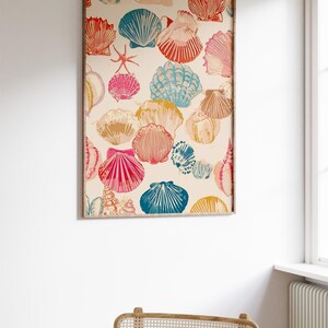 May include: A framed print featuring a repeating pattern of colorful seashells in shades of red, pink, blue, and yellow on a cream background. The artwork is displayed on a white wall, above a woven chair.