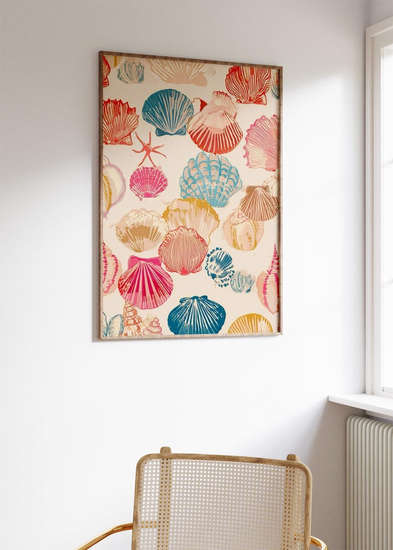May include: A framed print featuring a repeating pattern of colorful seashells in shades of red, pink, blue, and yellow on a cream background. The artwork is displayed on a white wall, above a woven chair.