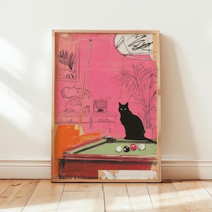 Puede incluir: Una impresión artística enmarcada que presenta un gato negro sentado en una mesa de billar con una superficie verde. La obra de arte tiene un fondo rosa con un dibujo de una lámpara, una planta y un taco de billar. La impresión está en un marco de madera.