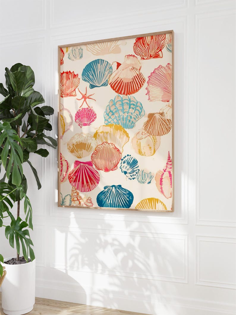 May include: A framed print featuring a repeating pattern of colorful seashells in shades of red, blue, pink, and yellow on a cream background. The artwork is displayed on a white wall, adding a coastal theme to the decor.