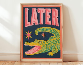 May include: A framed art print featuring a stylized alligator with an open mouth and the word "LATER" in pink letters. The alligator is yellow and green against a dark blue background, with two starbursts.