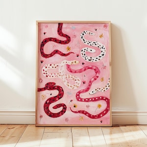 Op de afbeelding: Een ingelijste kunstdruk met een roze achtergrond. Verschillende slangen in rood, wit en roze tinten zijn afgebeeld, met patronen en vlekken. Kleine gele en witte bloemen zijn over het kunstwerk verspreid.