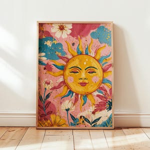 May include: A framed art print depicting a smiling sun with yellow rays and a face, set against a pink background with flowers and blue cloud accents. The artwork has a vintage, bohemian style, ideal for wall decor.