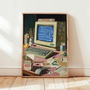 May include: A framed print depicting a retro computer setup on a pink desk. The monitor shows a blue graphic. A keyboard, mouse, and other desk items are present, including a food box with the word "TIGER". The word "NOVEMBER" is on the monitor.