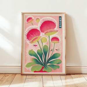 May include: A framed botanical print featuring a stylized illustration of Venus flytraps. The artwork showcases vibrant red and green hues, with the plants set against a soft pink background. Small insects are also depicted. The frame is made of light-colored wood.