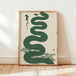 Könnte beinhalten: Gerahmter Kunstdruck mit einer stilisierten grünen Schlange auf cremefarbenem Hintergrund. Japanische Schriftzeichen und dekorative Elemente sind vorhanden. Das Kunstwerk befindet sich in einem Holzrahmen, geeignet für Wanddekoration.