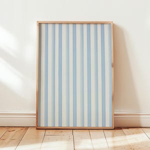 Peut inclure: Une œuvre d'art encadrée avec un motif à rayures verticales bleu clair et blanc. L'œuvre est dans un cadre en bois clair et est posée contre un mur blanc sur un sol en bois.