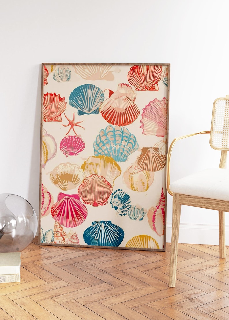 May include: A framed print featuring a pattern of colorful seashells in shades of red, pink, blue, and yellow on a cream background. The artwork is displayed in a room with a wooden floor and a chair.