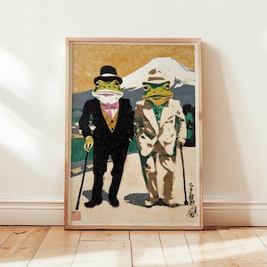 May include: Framed art print featuring two anthropomorphic frogs in suits and hats, standing in front of a mountain. One frog wears a black suit with a pink bow tie, the other a cream suit. The background has a vintage aesthetic.